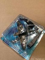 Photo of the diecast model aircraft and its plastic blister pack, showing the plane mounted securely on the curved black display stand. The packaging is worn but intact.
