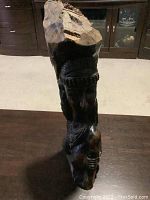 Front view of petrified wood carving on a table showing the carved female head with detailed jewelry and hair braids.