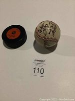 Photo of NHL official game puck and autographed baseball together on white surface with auction tag