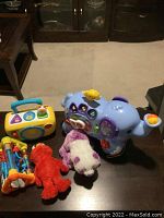 Photo showing a V-Tech elephant toy with multiple buttons, a Fisher-Price radio toy, and three plush toys, displayed on a table.