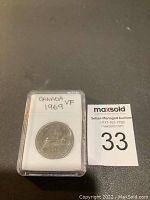 Photo shows a 1969 Canadian silver dollar coin contained in a clear plastic protective case labeled 'CANADA 1969 VF'. The coin surface details are visible under protective casing.