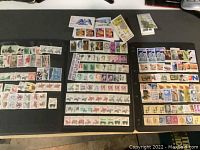 Photo showing multiple groups of mint USA stamps arranged on black surface, various denominations and designs