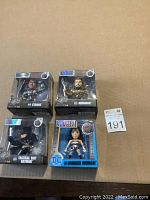 Four DC Metals die cast figures in original packaging: Tactical Suit Batman, Aquaman, Cyborg, Wonder Woman arranged on cardboard background.