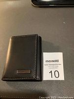 Closed view of the black leather tri-fold Tommy Hilfiger wallet showing the logo plaque.