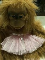 Front close-up view of orangutan puppet head and chest showing facial features and pink tutu detail.