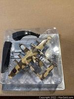 Top view of the scale model aircraft in blister pack with two-piece black display stand showing camouflage colors and RAF roundels on wings.