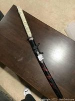 Full view of 36 inch replica Japanese katana sword in scabbard showing carved decorative handle and black/red dragon design scabbard.