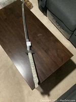 Full view of the katana resting on a dark wooden table showing the overall length and shape.