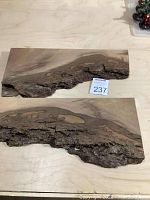 Two live edge walnut wood boards placed side by side on a light surface, showing natural bark edges and varying wood grain patterns.