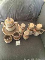 Full view of the vintage Laurentian Tundra Canada pottery tea set including teapot, creamer, sugar jar, plate, salt and pepper shakers, and two pourers arranged on a couch.