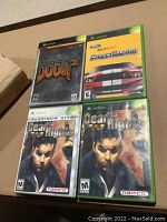 Five Xbox game cases on a cardboard surface including Dead to Rights, Dead to Rights Platinum Hits, Doom, Doom 3, and Ford Bold Moves Street Racing.