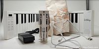 Foldable 88-key white digital piano with built-in speakers, control panel, and associated accessories including pedal, charging cord, and carrying case.