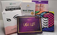 Photo showing six boxed beauty and self care items arranged in two rows on a blue surface, including foot exfoliation masks, wax strips, lash lift kit, false eyelashes, and magnetic eyelash kit.