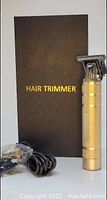 Hair trimmer standing upright next to black box labeled 'HAIR TRIMMER'. Charging cable coiled and wrapped in plastic.