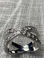 Front view of the sterling silver crossing band ring with cubic zirconia stones placed on grey textured fabric surface.
