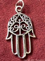 Front view of the 925 sterling silver Hamsa hand pendant placed on a red fabric background to show design details.