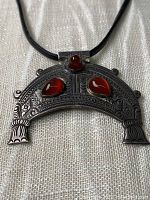 Front view of a hand-tooled sterling silver pendant with three polished carnelian cabochon stones set in bezel settings, hanging on a black cord necklace.