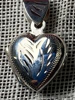 Front close-up of heart-shaped sterling silver locket pendant showing engraved leaf details.
