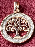 Close-up photo of front of pendant showing rose gold tree within sterling silver textured ring on red fabric.
