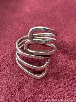 Close-up view of the silver wrap-around ring showing the open design with three curved parallel bands and polished finish.