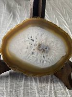 Full view of polished agate slice displaying beige outer edge and white crystal interior in wooden stand