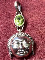 Close-up image of the pendant showing faceted oval peridot gemstone with a bezel silver setting and the Buddha face below.