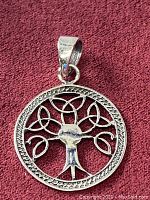 Front view of round 925 sterling silver Celtic Tree of Life pendant with triquetra leaf design and textured border on burgundy fabric background.