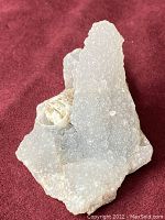 Front view of rough chalcedony crystal showing vertical projection and granular texture on a red cloth background.