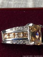 Close-up of faceted CZ and sterling silver ring from side angle showing channel set square stones and round stones on band.