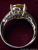 Side view of sterling silver ring showing the cut-out design and prong setting of the yellow round stone.