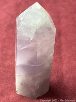 Front view of six-sided polished fluorite crystal point on red background.