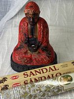 Front view of red and black ceramic Buddha incense burner with the incense stick boxes positioned in front