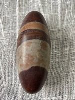 Top view of the Lingum sacred stone showing its elongated oval shape with distinct earth-tone horizontal bands.