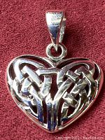 Close up front view of the heart-shaped Celtic knot pendant showing detailed polished interlaced silver design on a red fabric background.