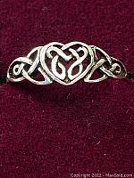 Close-up of front face of the sterling silver ring showing detailed Celtic knot heart design on a maroon fabric background.