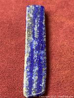 Polished lapis lazuli stone on red fabric, showing vibrant blue with calcite and pyrite inclusions.