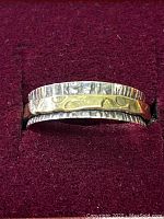 Close up front view of sterling silver ring with hammered finish and brass band on red velvet background.