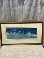 Framed picture of a winter scene showing a rabbit sitting in snow beneath tree branches. Brown frame and white mat visible.