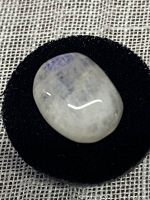 Close-up photo of oval, polished, translucent moonstone cabochon with visible internal striations placed on black cloth.