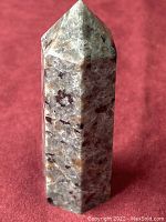 Front view of six-sided pointed Mystic Merlinite tower crystal on a red background.