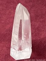 Clear quartz crystal point with natural phantom inner formations, standing upright on a burgundy fabric.