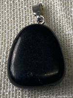 Front view of triangular polished black shungite pendant with silver-tone bail on fabric background