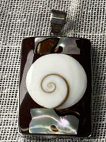 Front view of rectangular pendant showing central circular Shiva eye shell and two iridescent shell inlays on a black base.