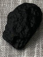 Close-up of the black tektite showing rough irregular surface on woven fabric background.