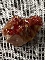 Close-up photo showing orange hexagonal Vanadanite crystals clustered on a light mineral matrix on a textured fabric background.
