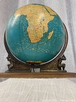 Front view showing globe facing Africa, wooden base, twin Atlas figures