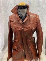 Full front view of the brown leather coat displayed on mannequin with black and white patterned scarf.