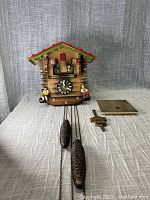 Overall view of cuckoo clock with two pine cone weights, pendulum and back panel laid out.