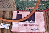 Three quilting books by Helen Squire and one wooden embroidery hoop arranged on a carpet.