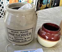 Photo showing large ceramic jug with 'Home Made Preserves' label and small brown and cream pot.